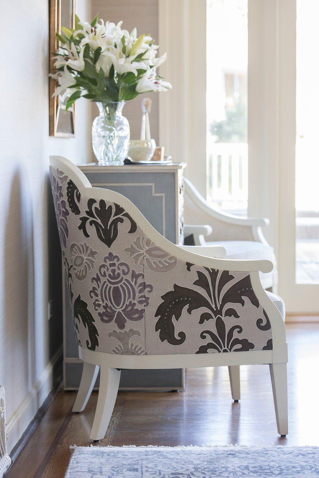 Elegant patterned chair with a floral arrangement in a bright room.