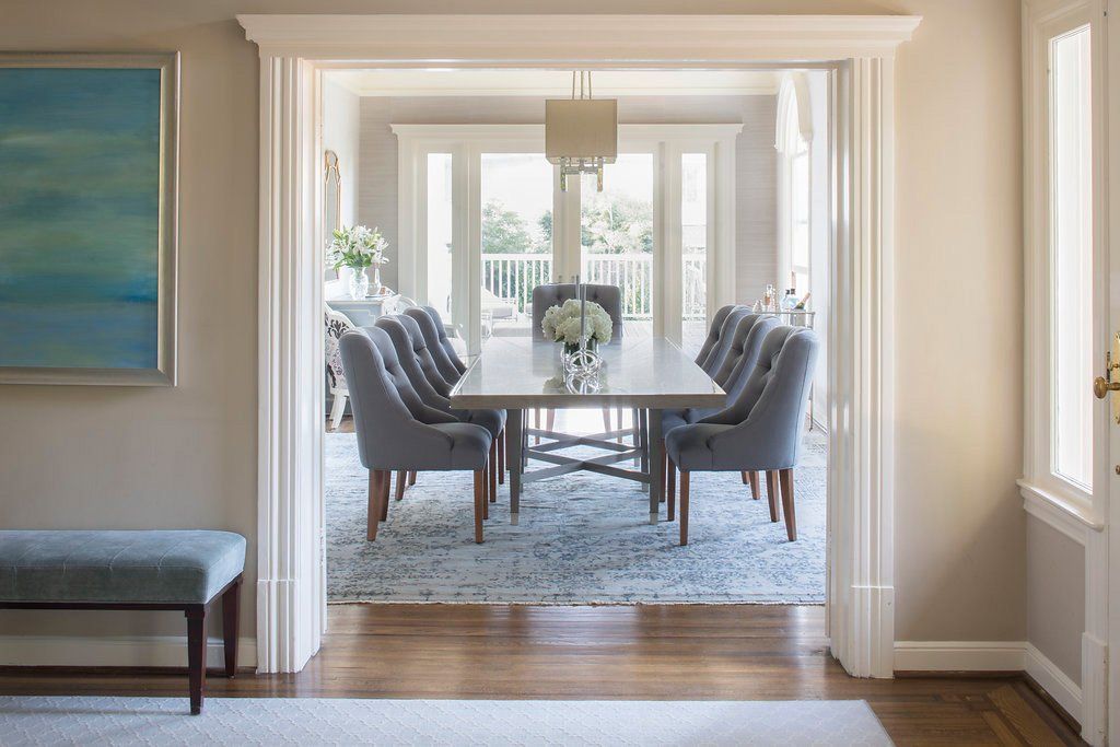 Dining room: Long table with gray chairs, rug, and balcony view, seen through doorway.