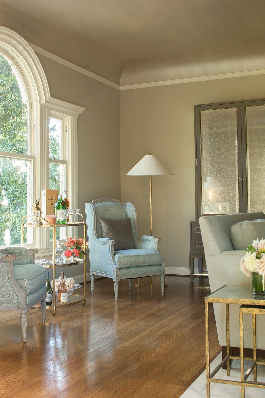 Elegant living room with blue armchairs, gold accents, and a large arched window.