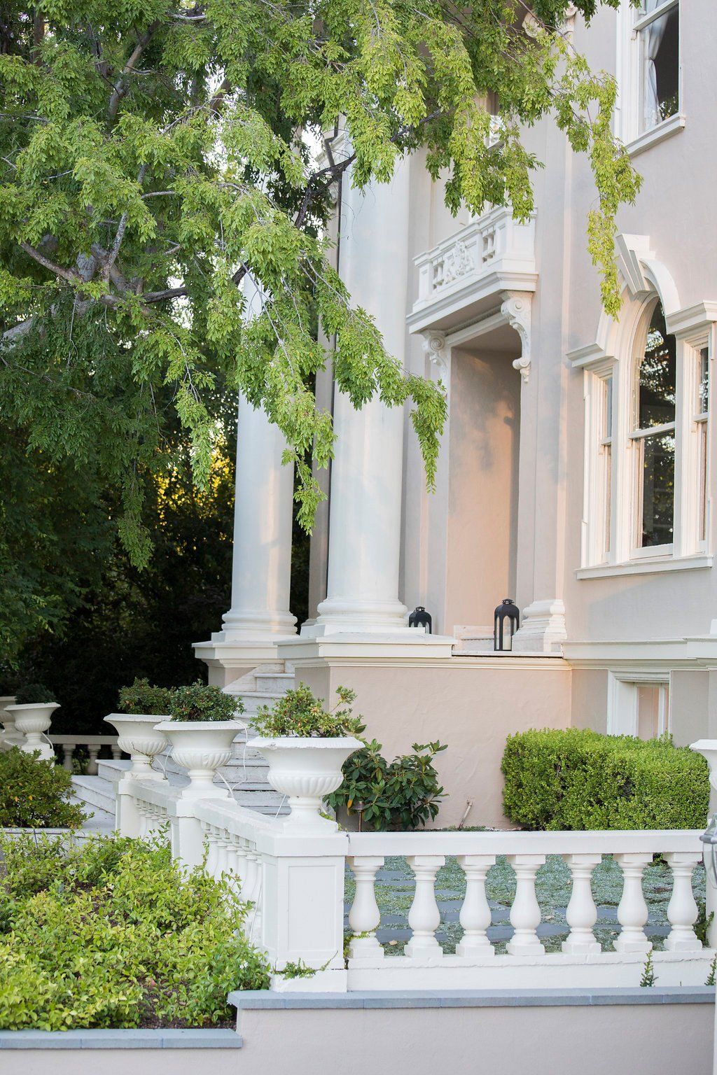 Exterior of a large, white building with columns and a decorative balustrade, with lush greenery.
