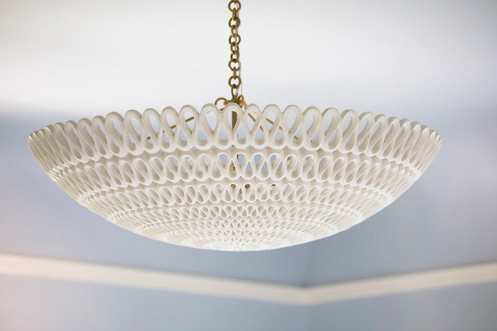 White, woven-style chandelier hangs from a gold chain on a light blue ceiling.