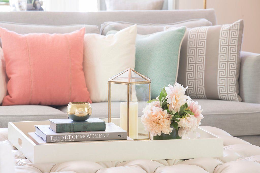 Gray sofa with colorful pillows, a white tray with books, candles, and flowers on a tufted ottoman.