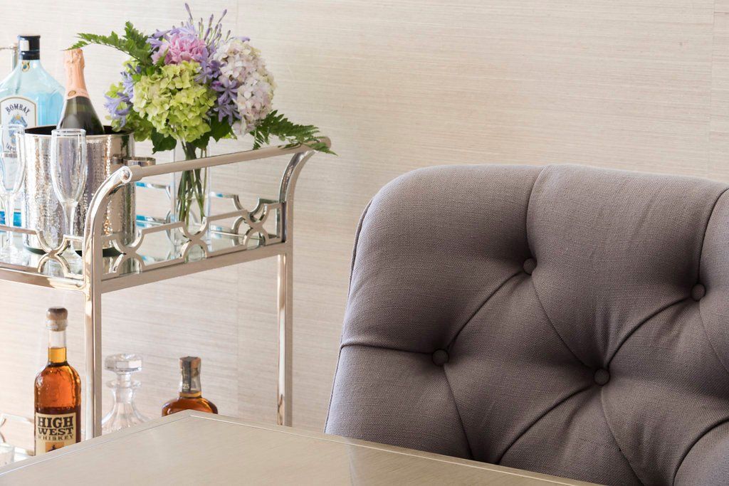 Bar cart with bottles, champagne, flowers, and a tufted chair.