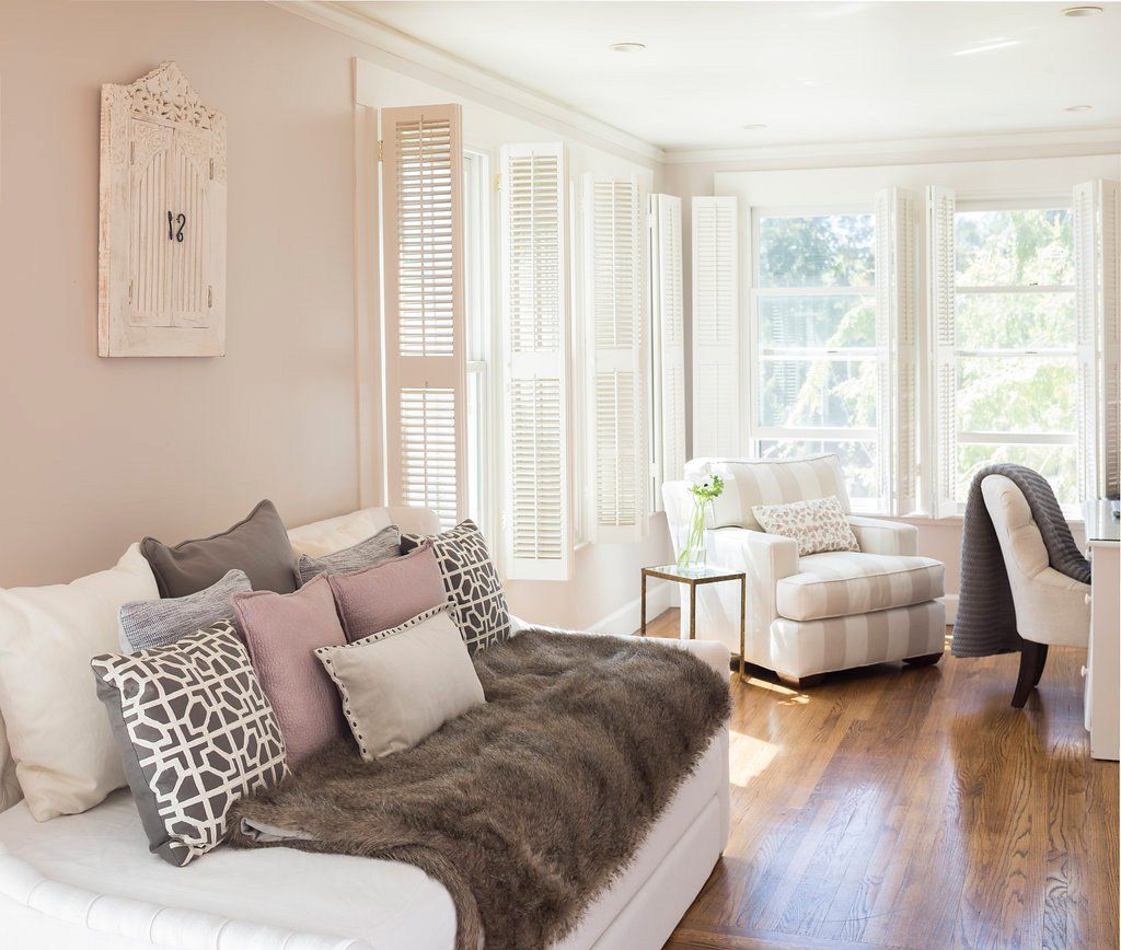 Living room with white walls, shutters, and furniture, featuring a daybed with pillows and a fur throw.