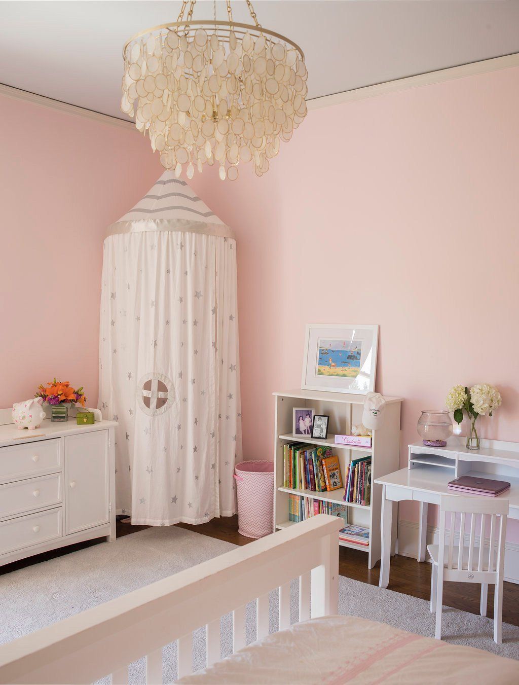 Pink bedroom with chandelier, canopy, dresser, desk, bookshelf, and a bed.