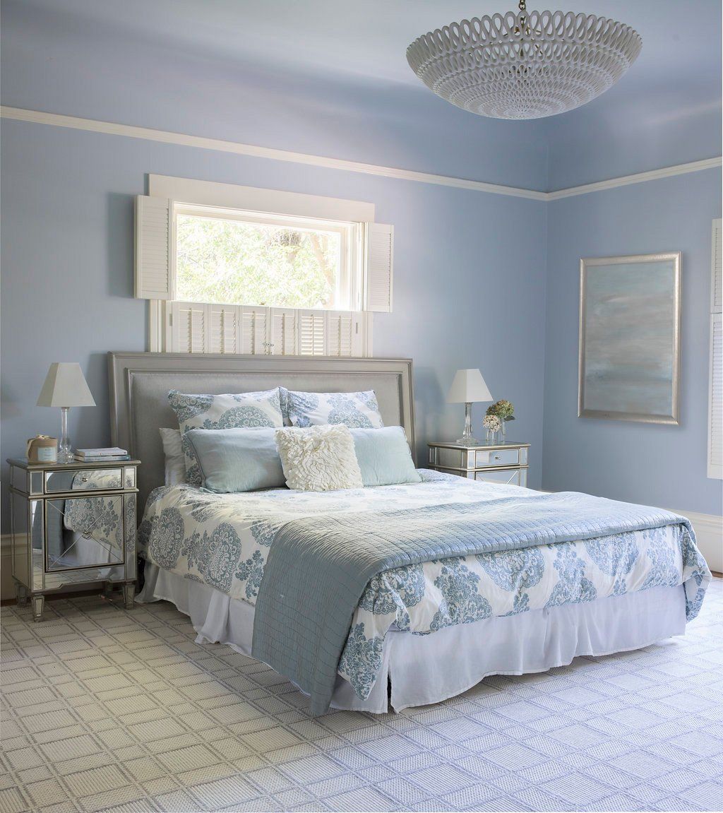 Bedroom with blue walls, bed with floral bedding, mirrored nightstands, and a crystal chandelier.