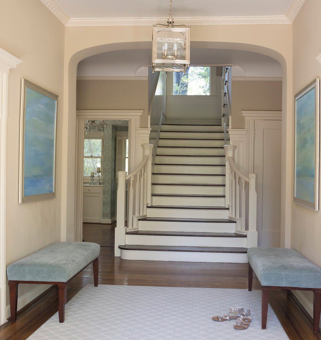 Hallway with stairs, benches, and artwork. Beige walls, wood floors, light blue benches and art.