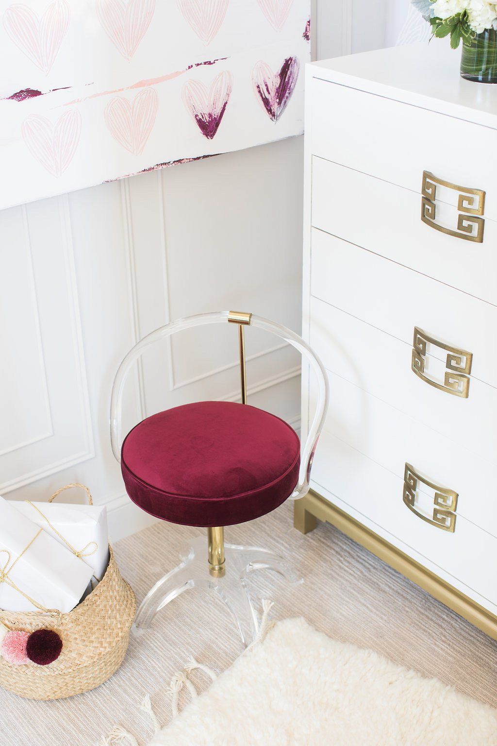 A child's room with a red velvet chair, white dresser, and heart-patterned bedding.