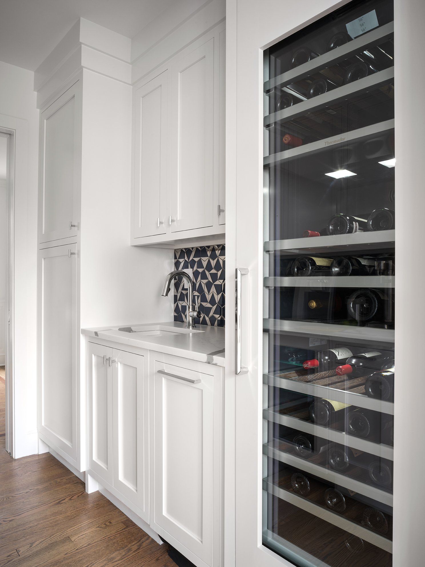 White built-in bar area with wine fridge and sink, featuring cabinets and a patterned backsplash.