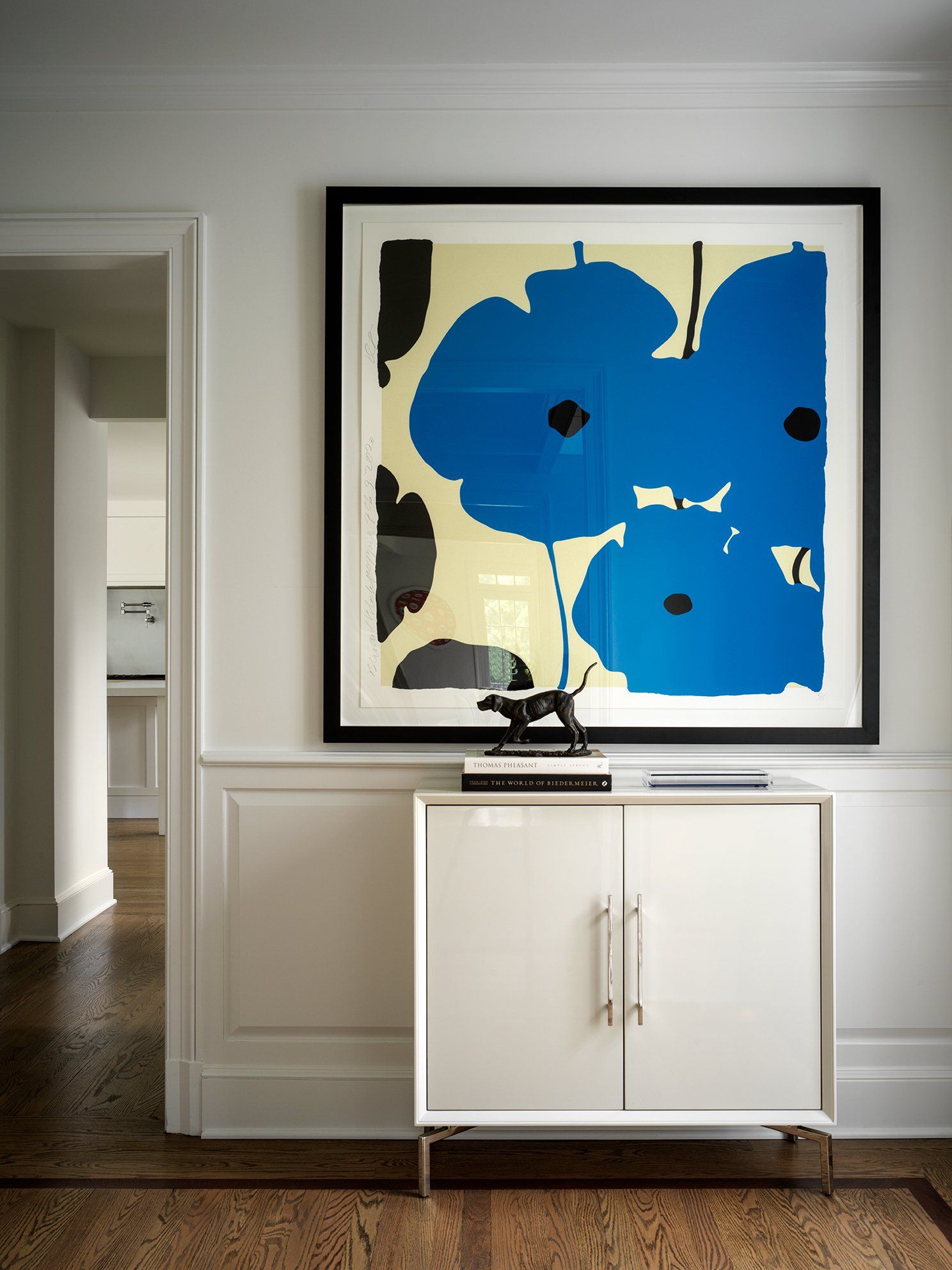 White cabinet with artwork of blue flowers on a wall. Entryway with wooden floor.