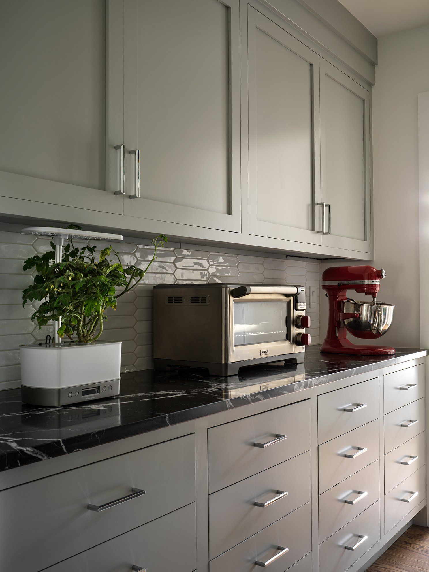 Gray kitchen cabinets with a black countertop, a red mixer, a toaster oven, and a plant.