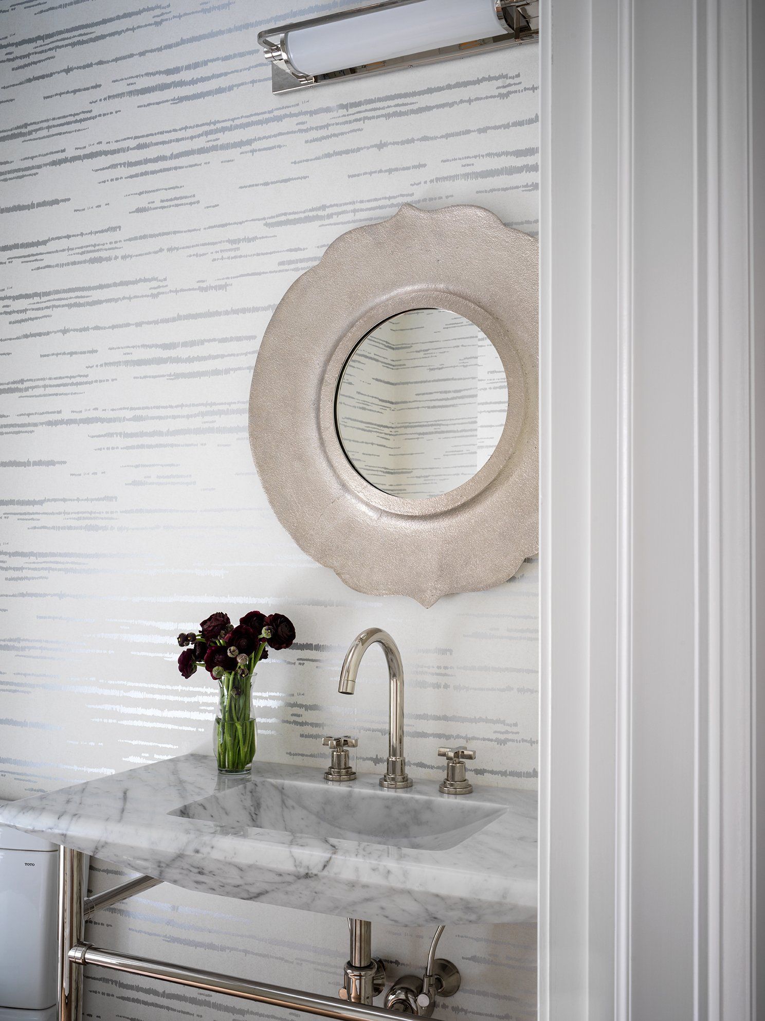 Bathroom with silver mirror, marble countertop, and decorative wallpaper.