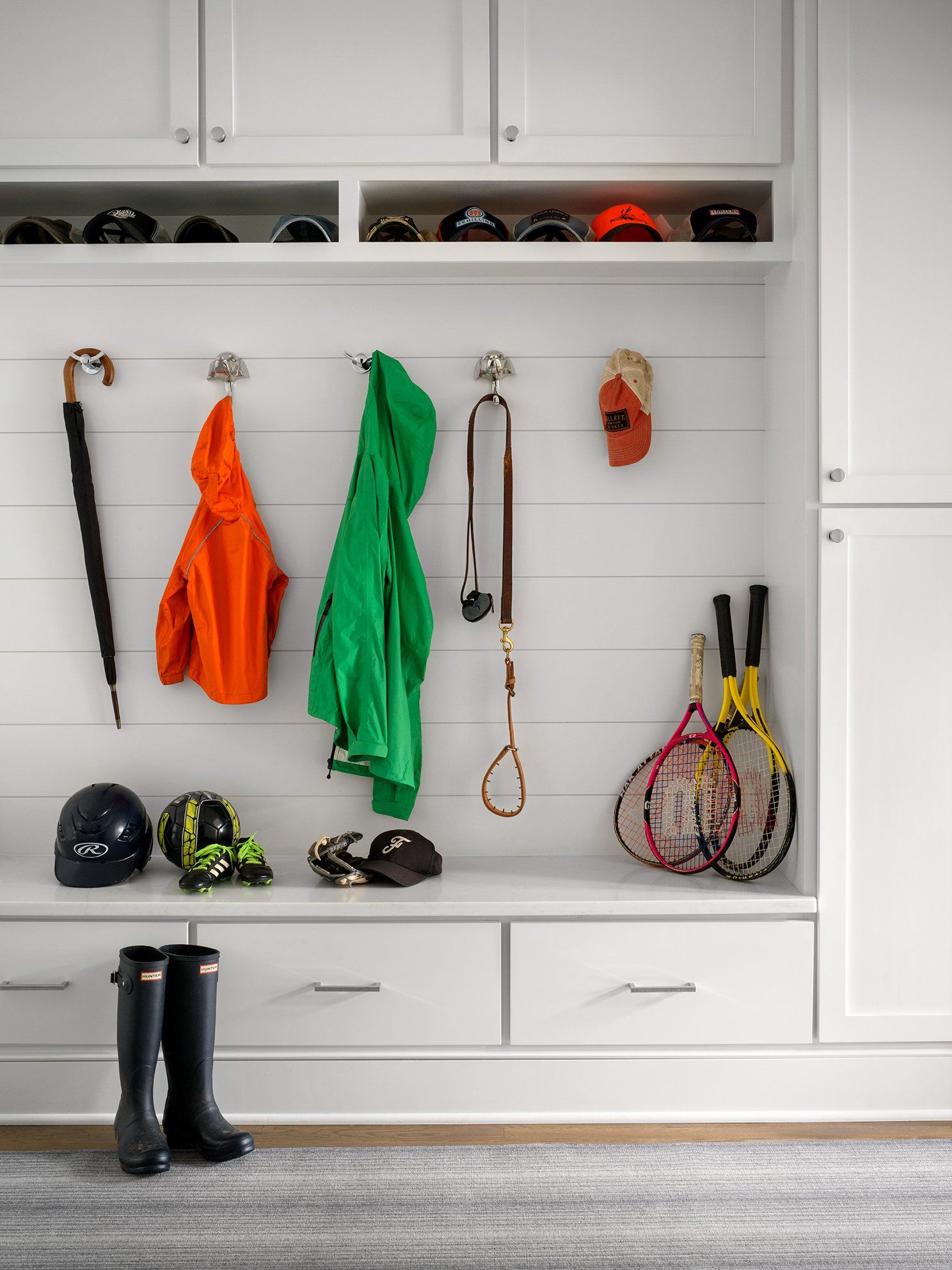 White mudroom with hooks holding coats, accessories, and shoes. Storage above and below.