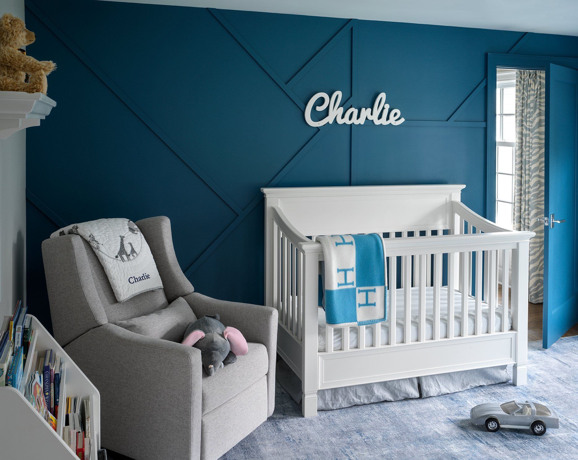 Nursery with blue accent wall, white crib, gray chair, and name 