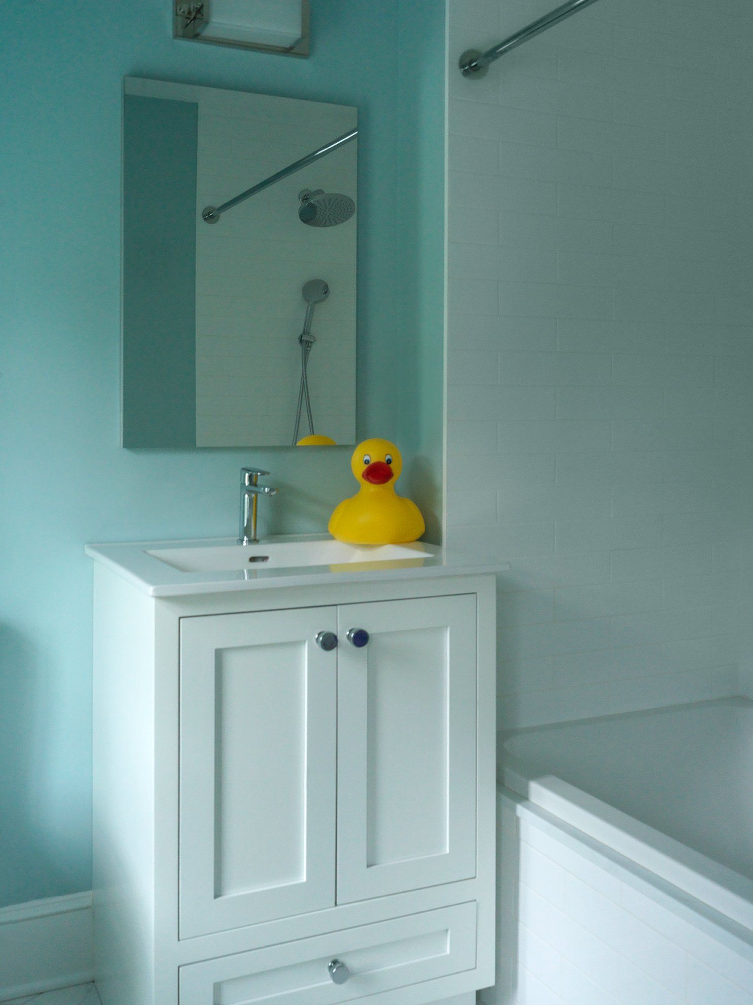 White bathroom vanity with a yellow rubber duck, mirror, and shower. Blue walls.