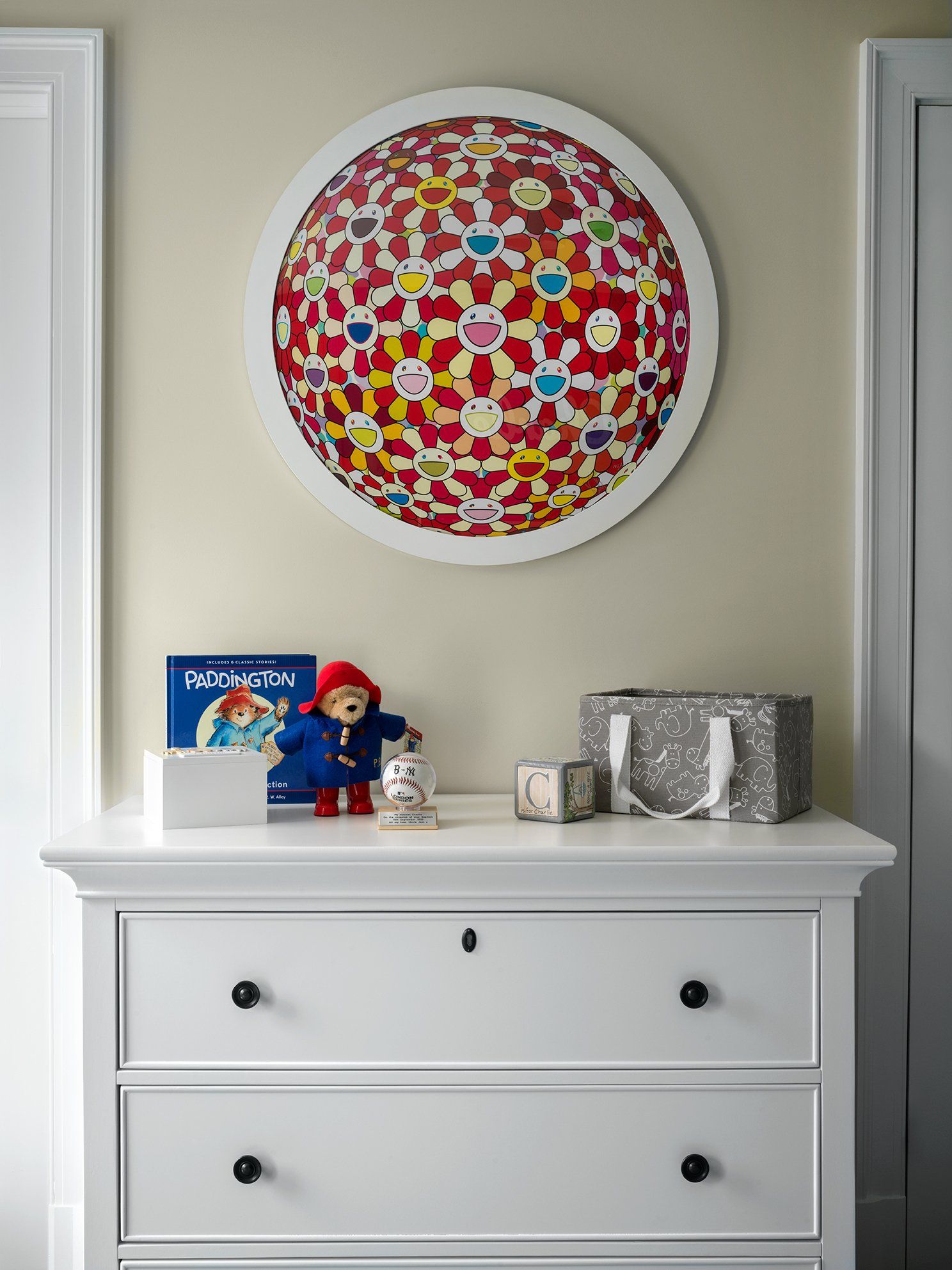 White dresser with art, books, and stuffed animal below a colorful, pixelated circle on a beige wall.