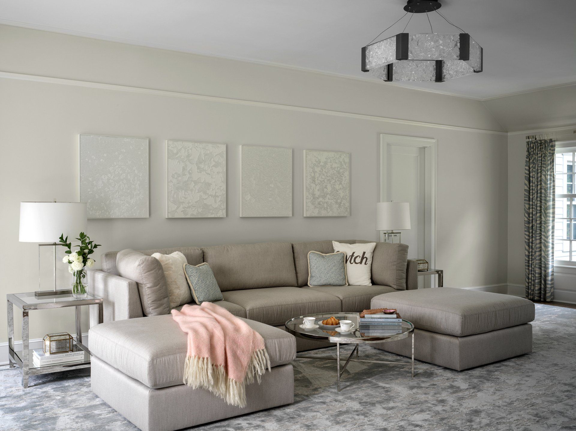 Neutral-toned living room with a sectional sofa, ottomans, artwork, and a patterned rug.