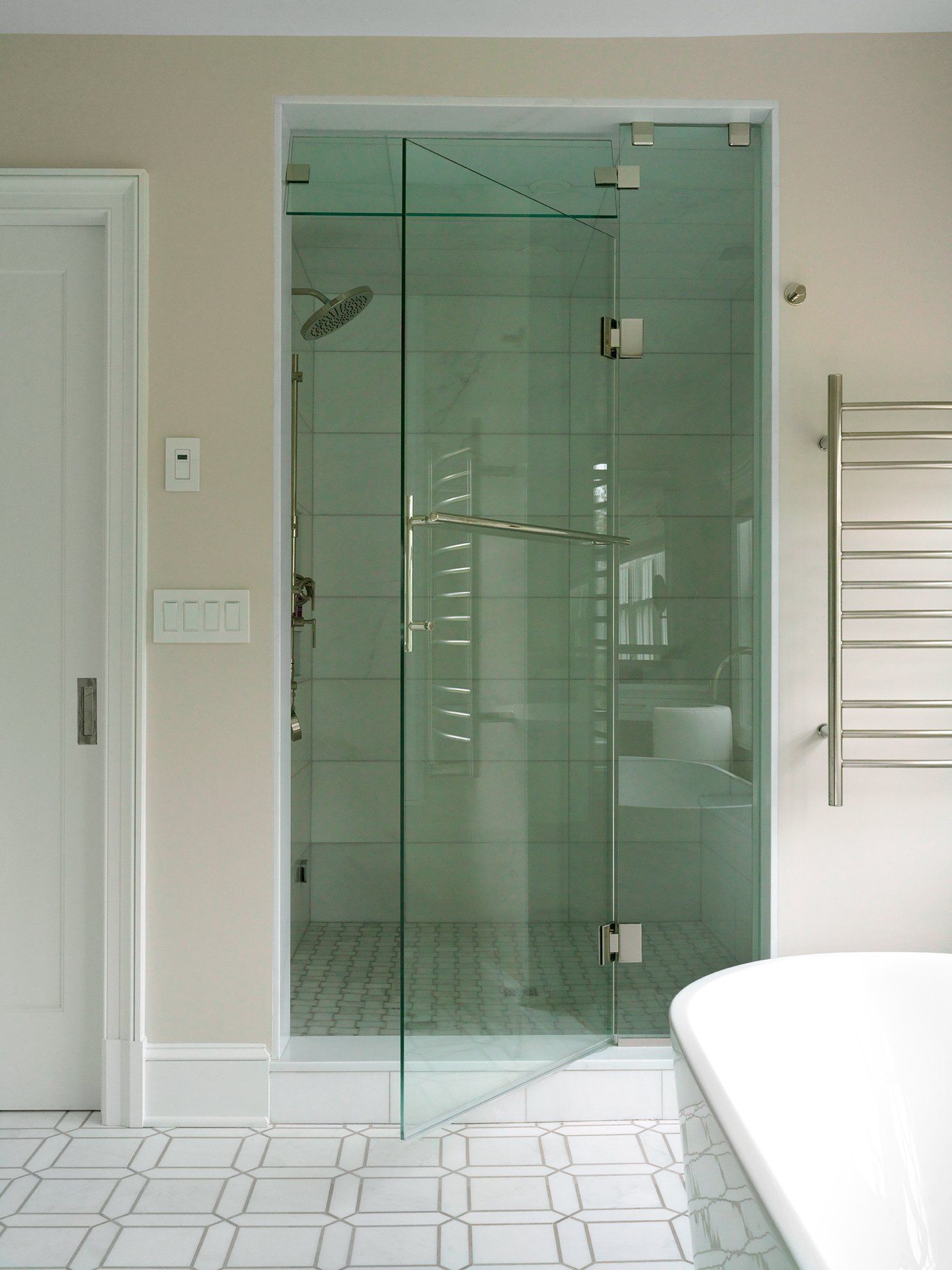 Glass shower enclosure in a bathroom with white and gray tile floor.