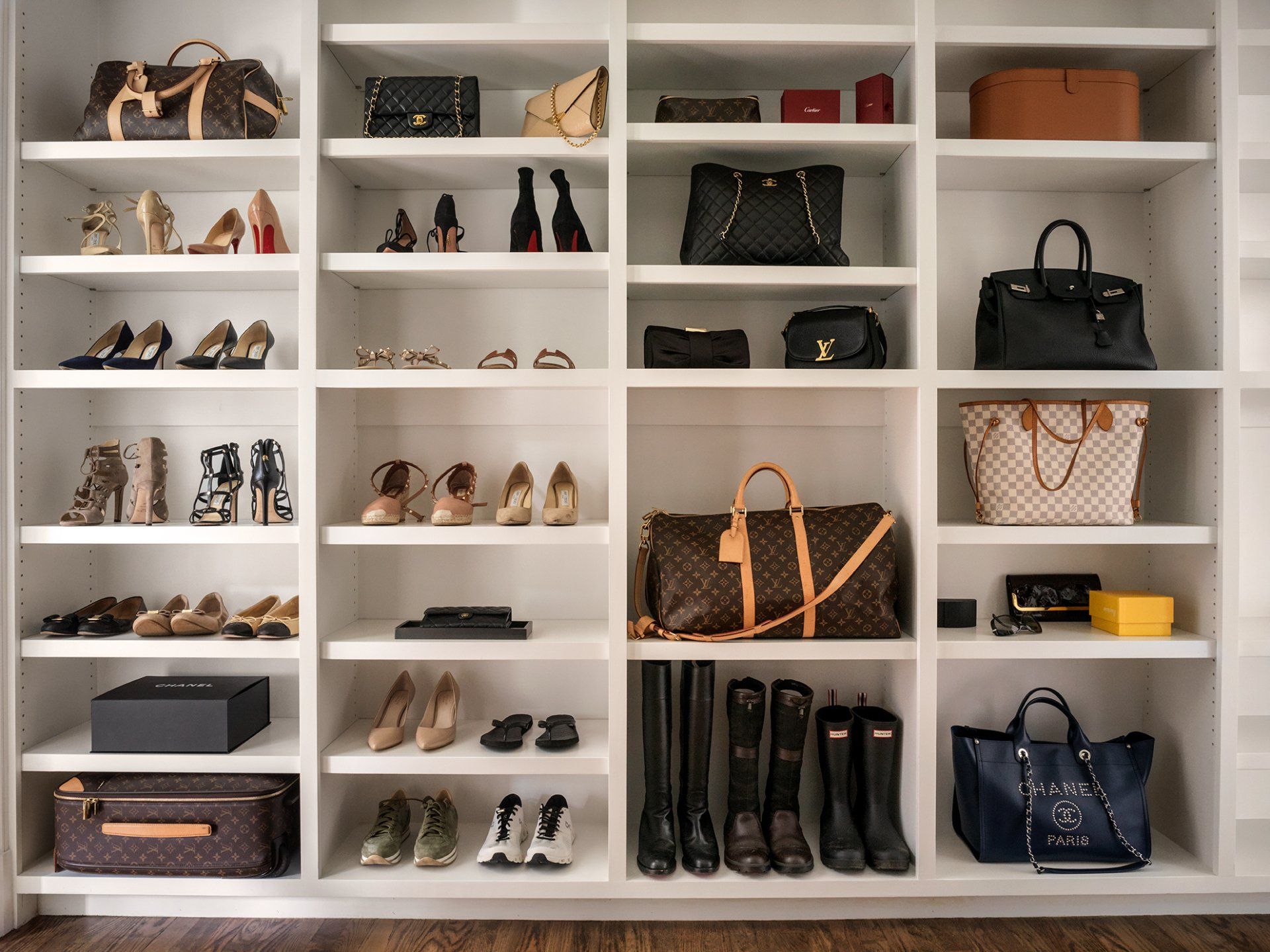 White built-in shelves display designer handbags, shoes, and accessories in various colors and styles.