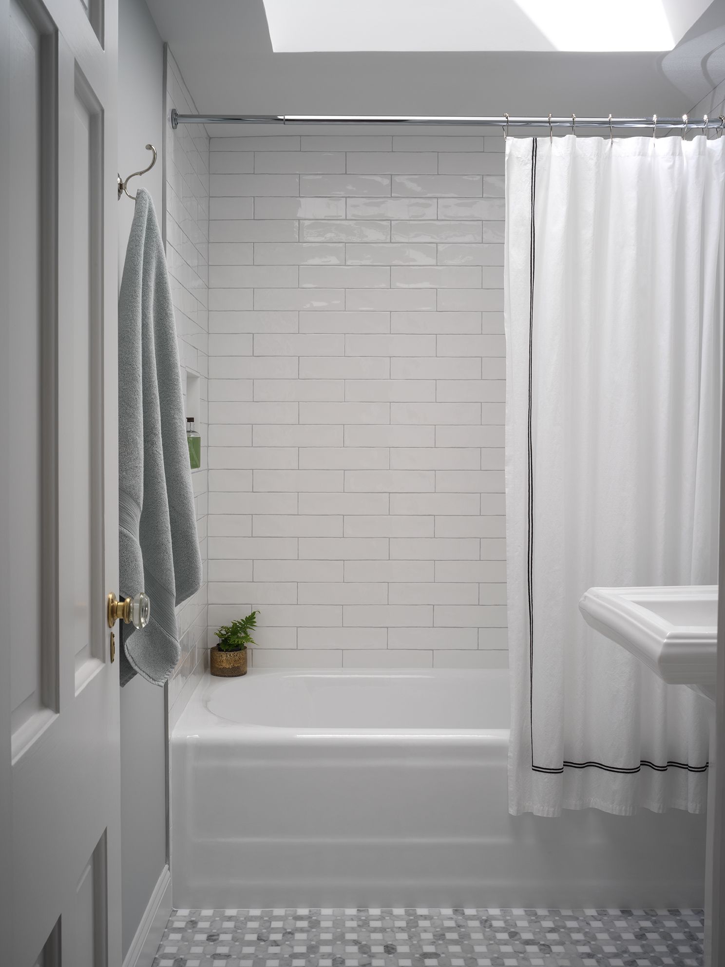 Small, white bathroom with tub, subway tile, curtain, sink, and gray towel.