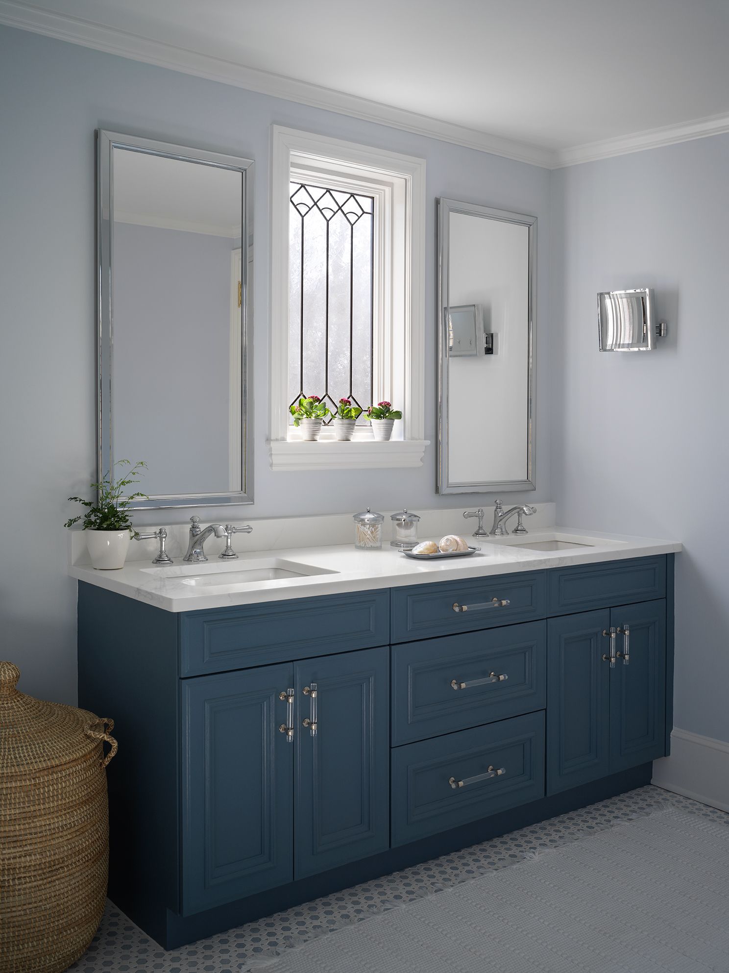 Blue bathroom vanity with mirrors, window, and wicker basket.