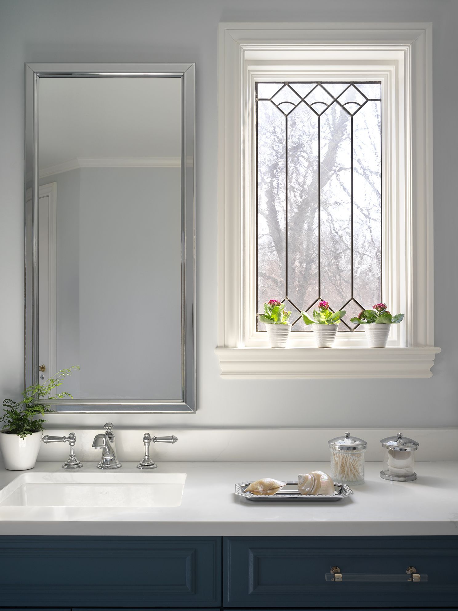 Bathroom with mirror, window with stained glass, flowers on the sill, and countertop.