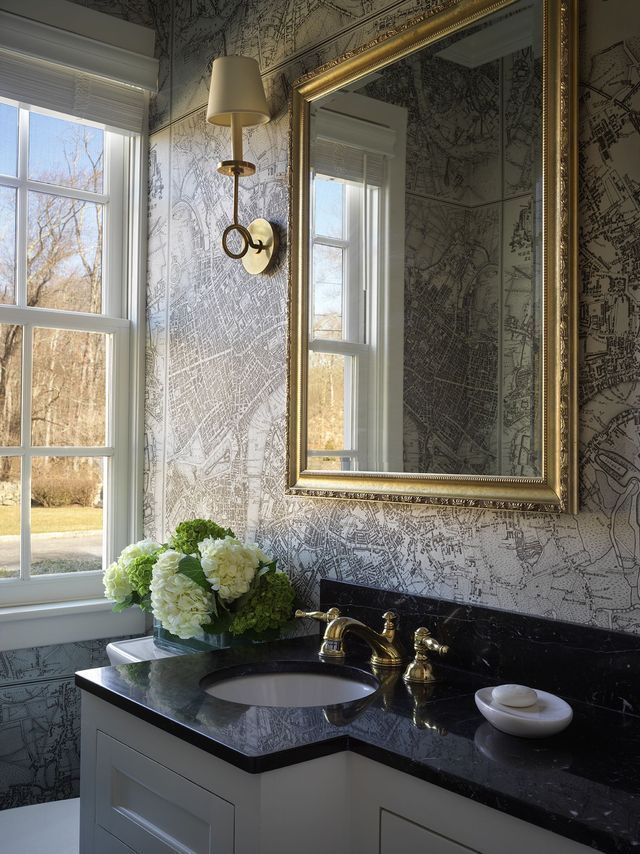 Bathroom with gold-framed mirror, floral arrangement, gold fixtures, and patterned wallpaper.