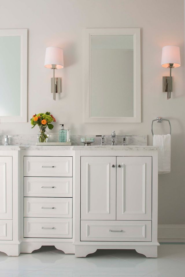 White bathroom vanity with two mirrors, sconces, and a flower arrangement.