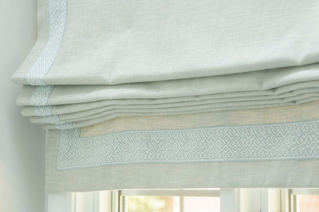 Light blue Roman shade with decorative trim, partially closed over a window.