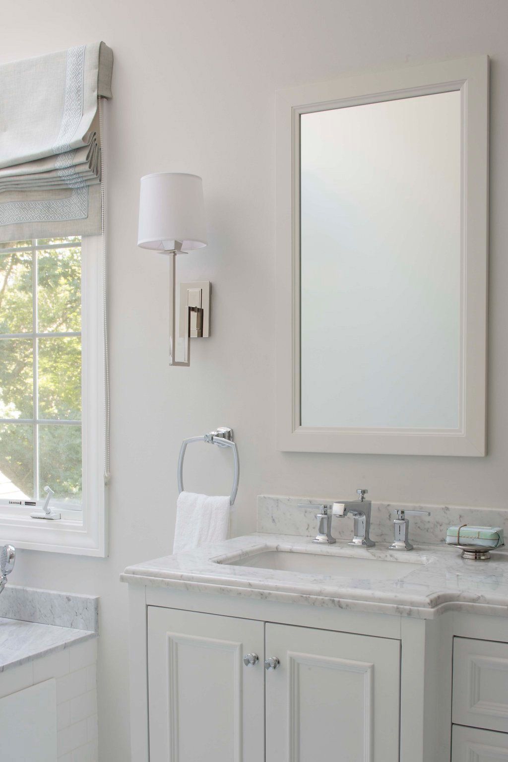 White bathroom with marble countertop, sink, mirror, and wall-mounted lamp.