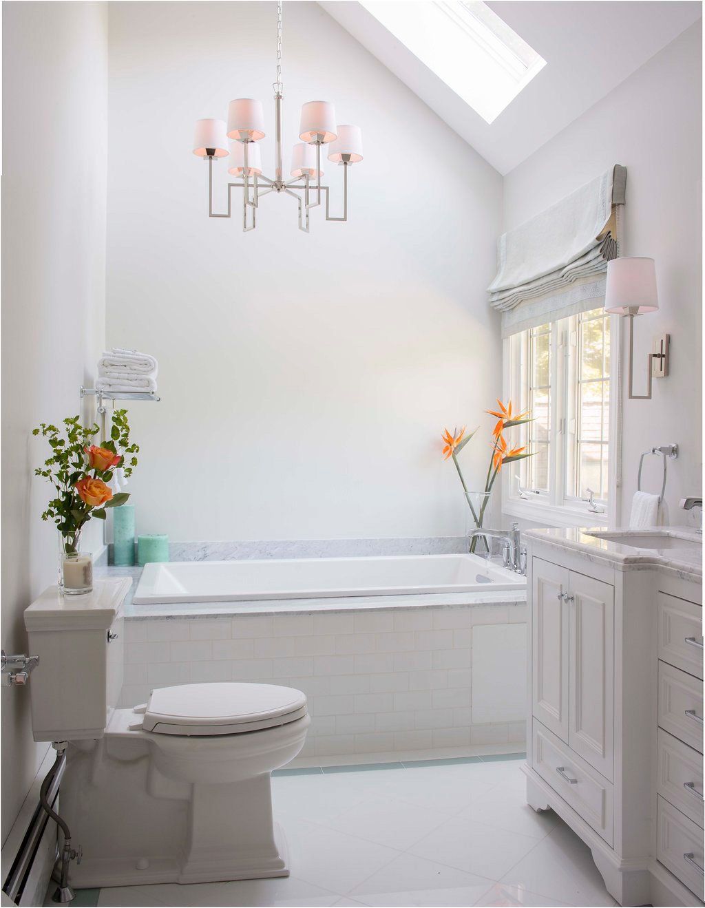 White bathroom with a bathtub, toilet, vanity, and a chandelier.
