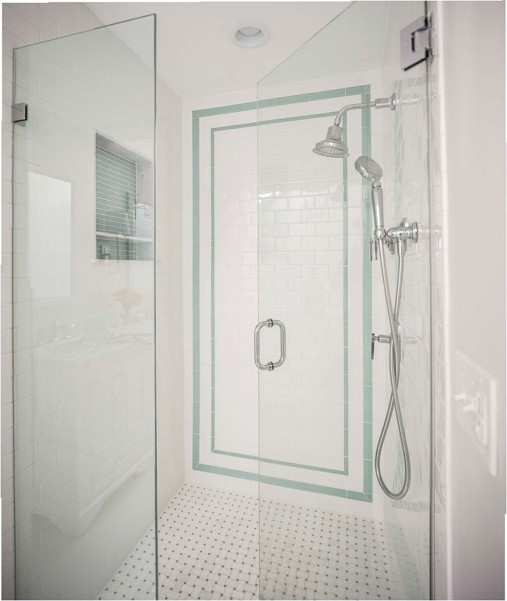 Glass shower enclosure with white subway tile and a decorative border.