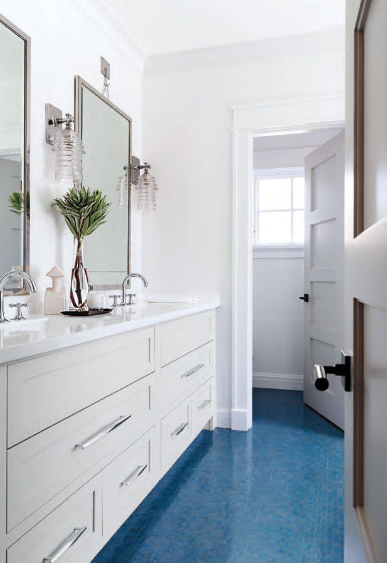 White bathroom with blue floor, double vanity, mirrors, and open door.