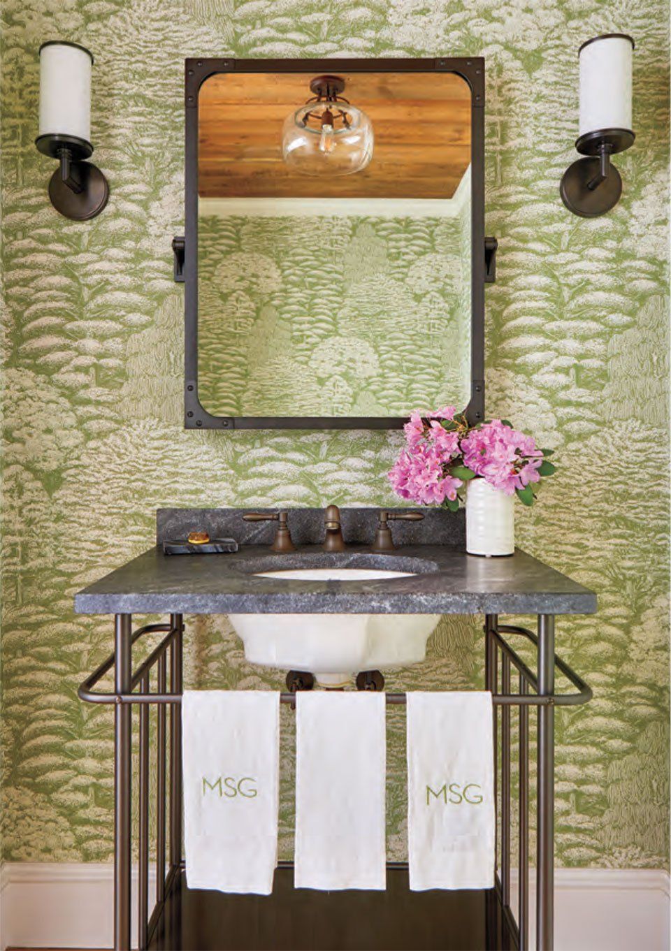 Bathroom with green patterned wallpaper, dark framed mirror, metal sink stand, and white towels.