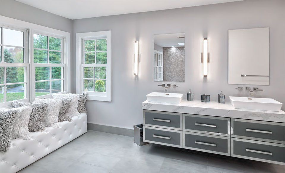 A modern bathroom with a double vanity, large windows, and gray and white decor.