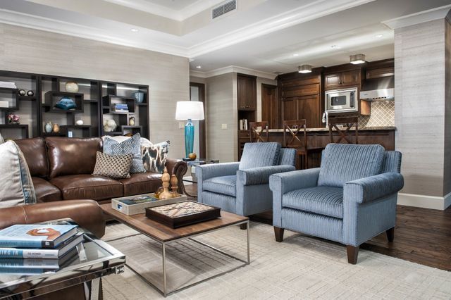 Living room with leather sofa, blue armchairs, open kitchen, neutral tones, and light wood floors.