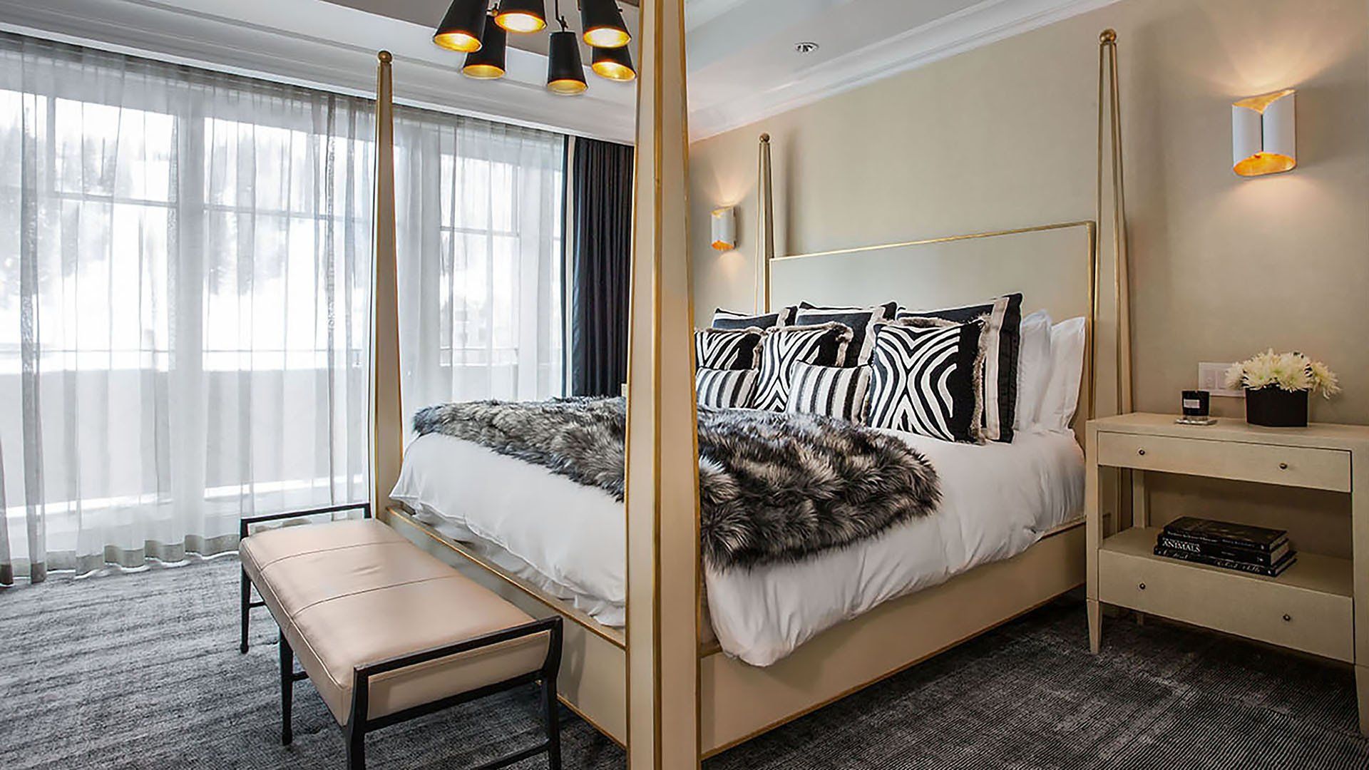 Bedroom with a four-poster bed, zebra-print pillows, faux fur throw, window, and a bench.
