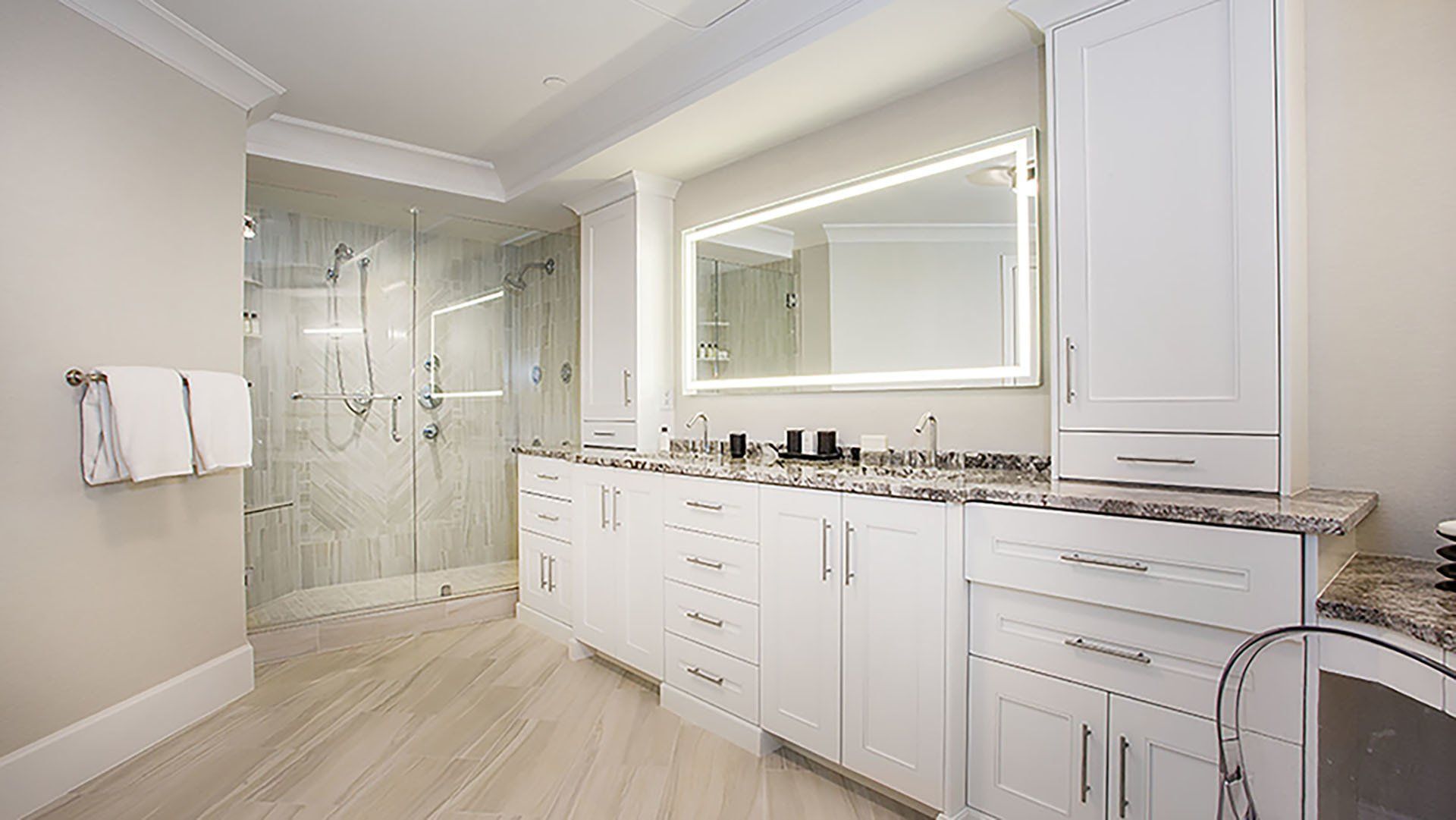 Bright, white bathroom with a large vanity, lighted mirror, and glass shower.