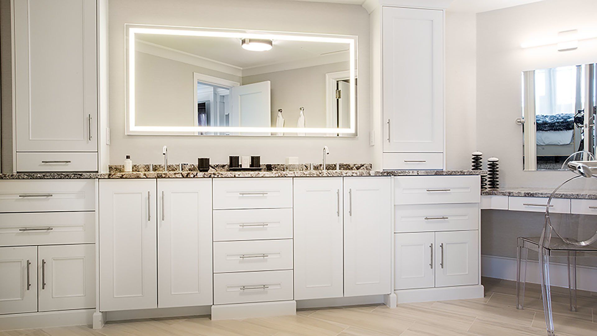 White vanity with lighted mirror, granite countertop, and matching cabinets in a well-lit room.