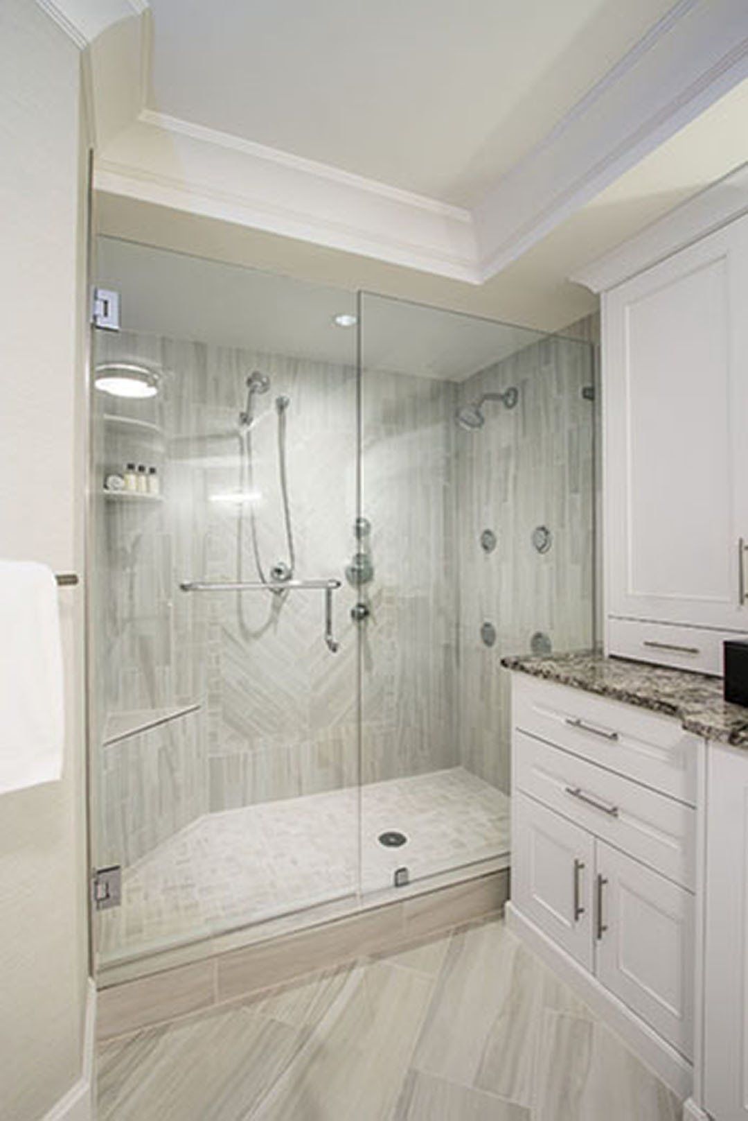 Modern bathroom with a glass shower enclosure and white cabinets. Gray tile floor and walls.