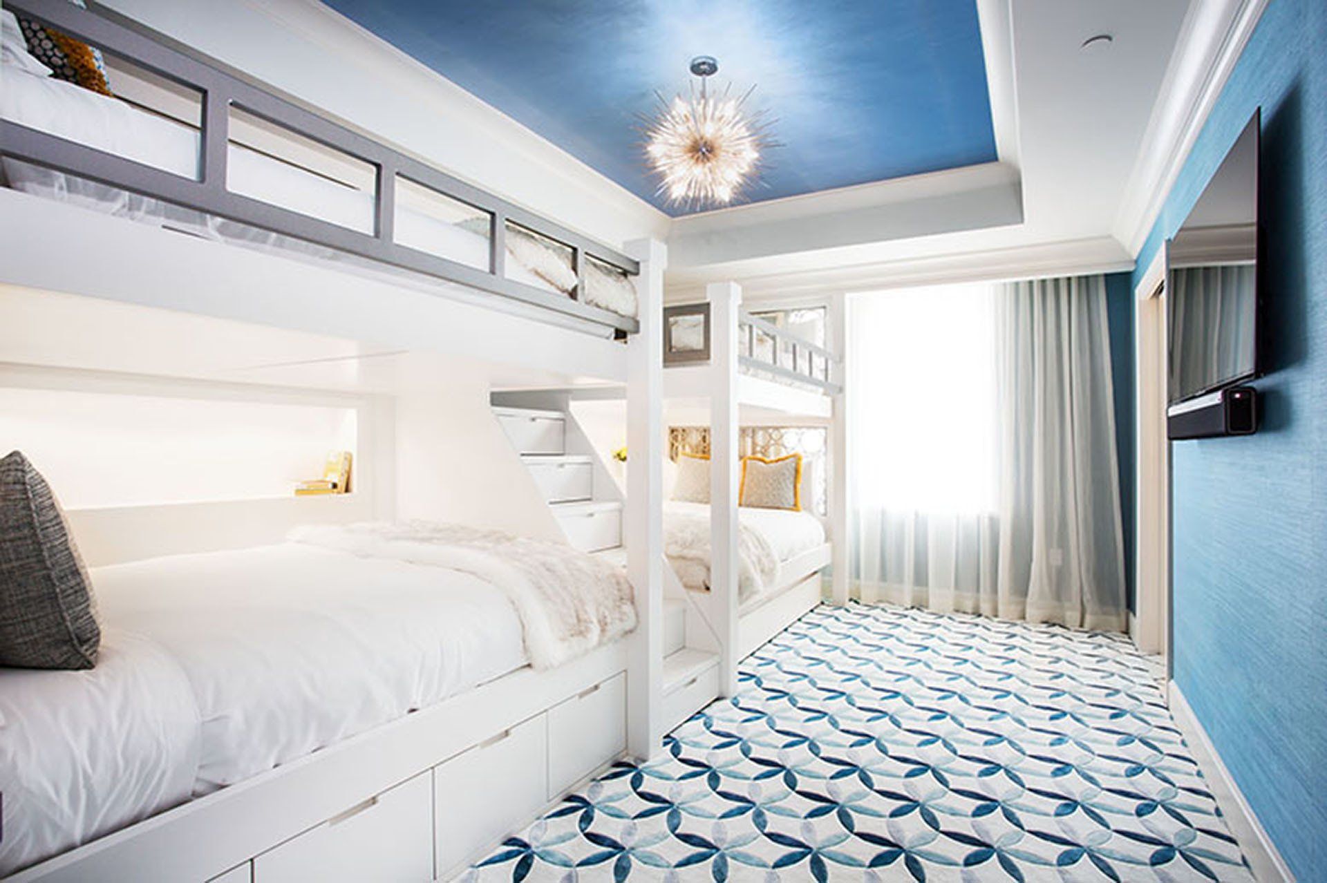 White bunk beds in a blue and white room with a patterned rug and chandelier.