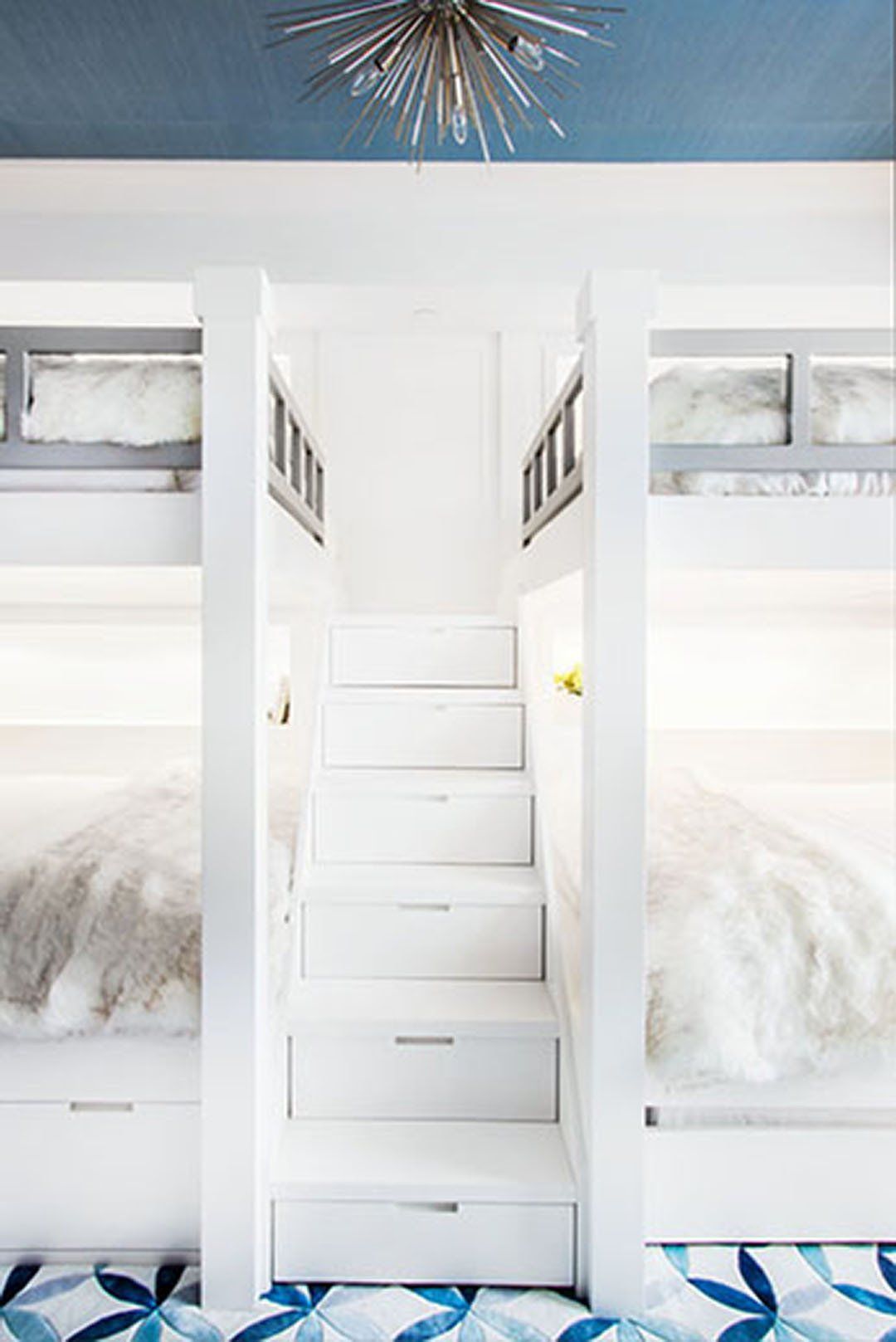 White bunk beds with built-in stairs, centered beneath a blue ceiling with a sputnik chandelier.