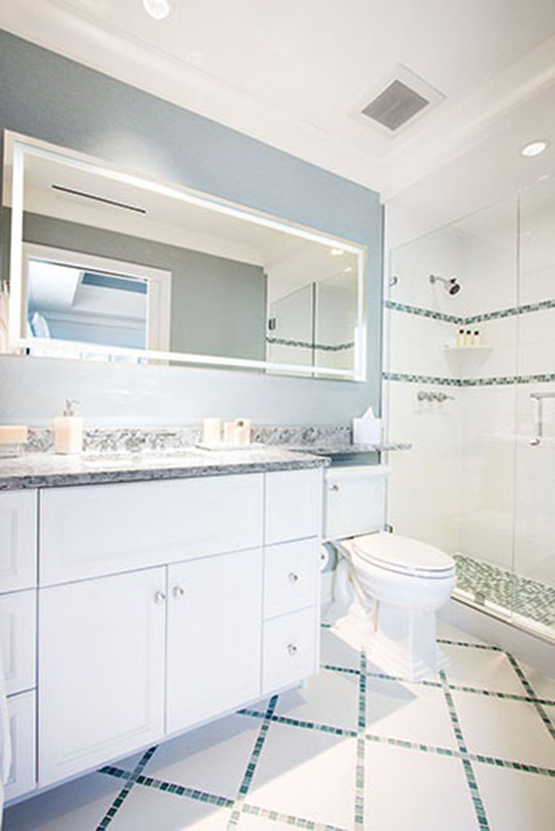 Bathroom with white cabinets, blue walls, large mirror, glass shower, and patterned tile floor.