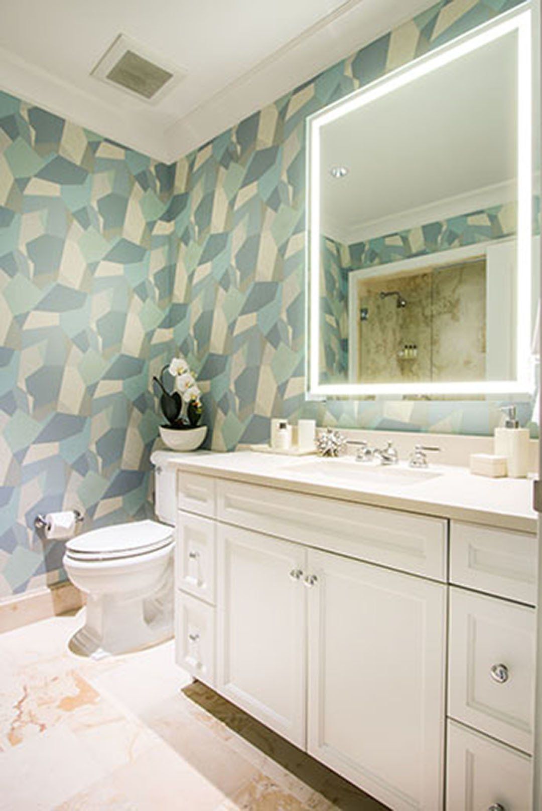 Bathroom with white vanity, patterned blue and white wallpaper, and large mirror with lit frame.