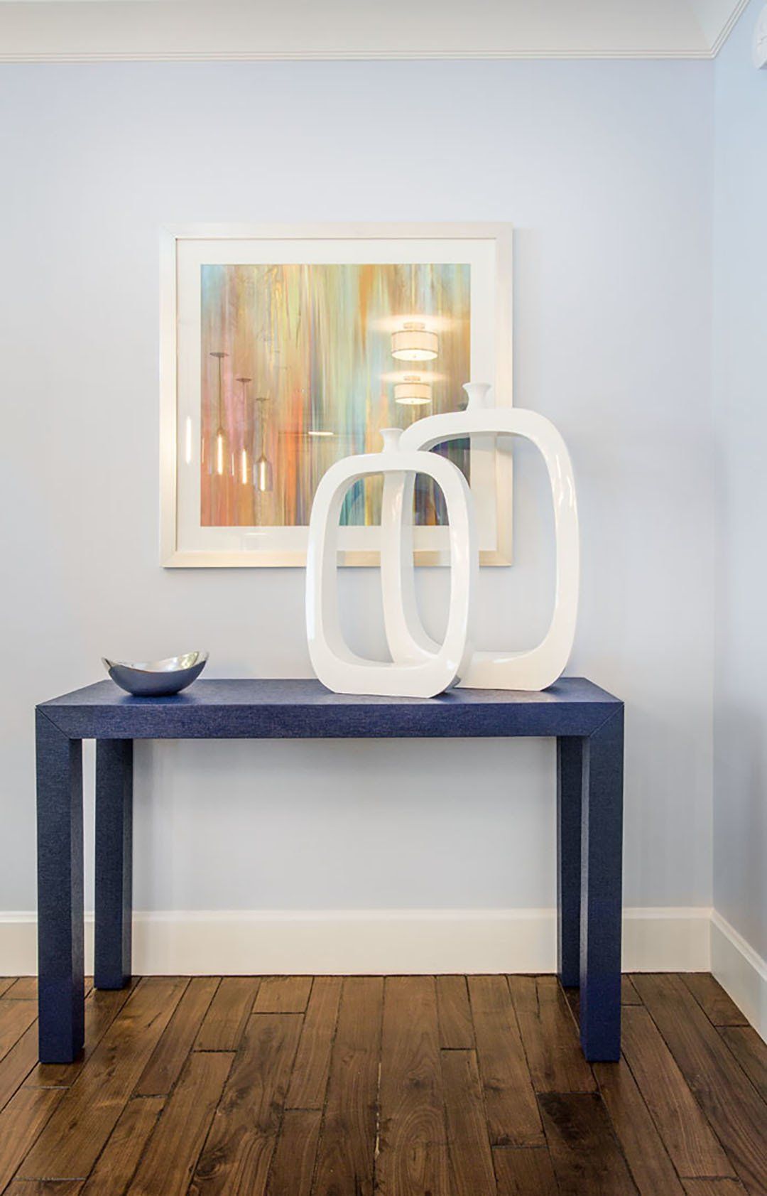Blue console table with white decor and abstract art on a light blue wall.