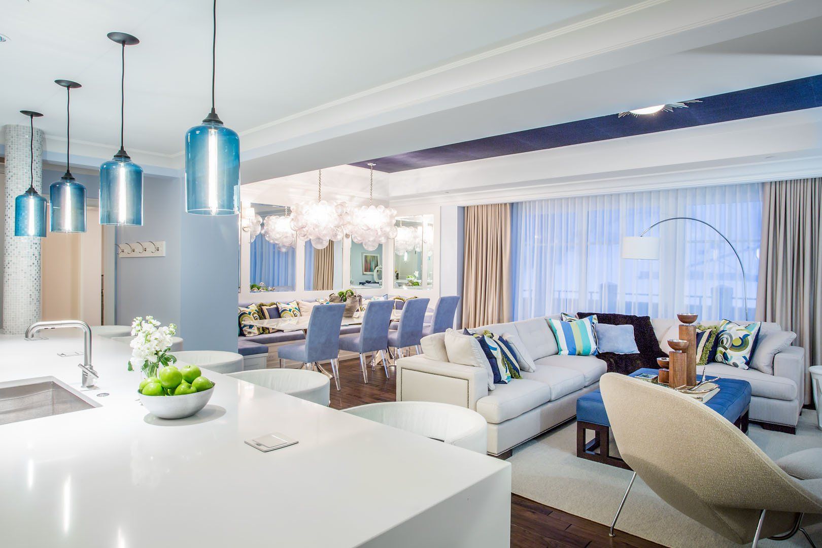 Open-concept living space with a white kitchen, dining area, and seating. Blue and neutral tones.