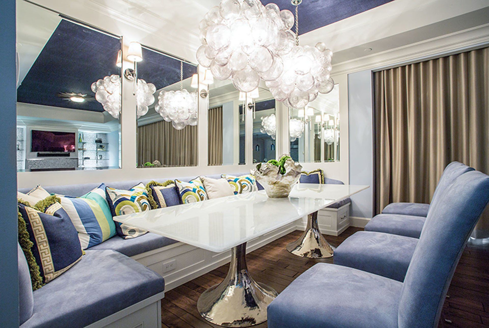 Dining room with a blue banquette, white table, and crystal chandeliers reflected in mirrors.