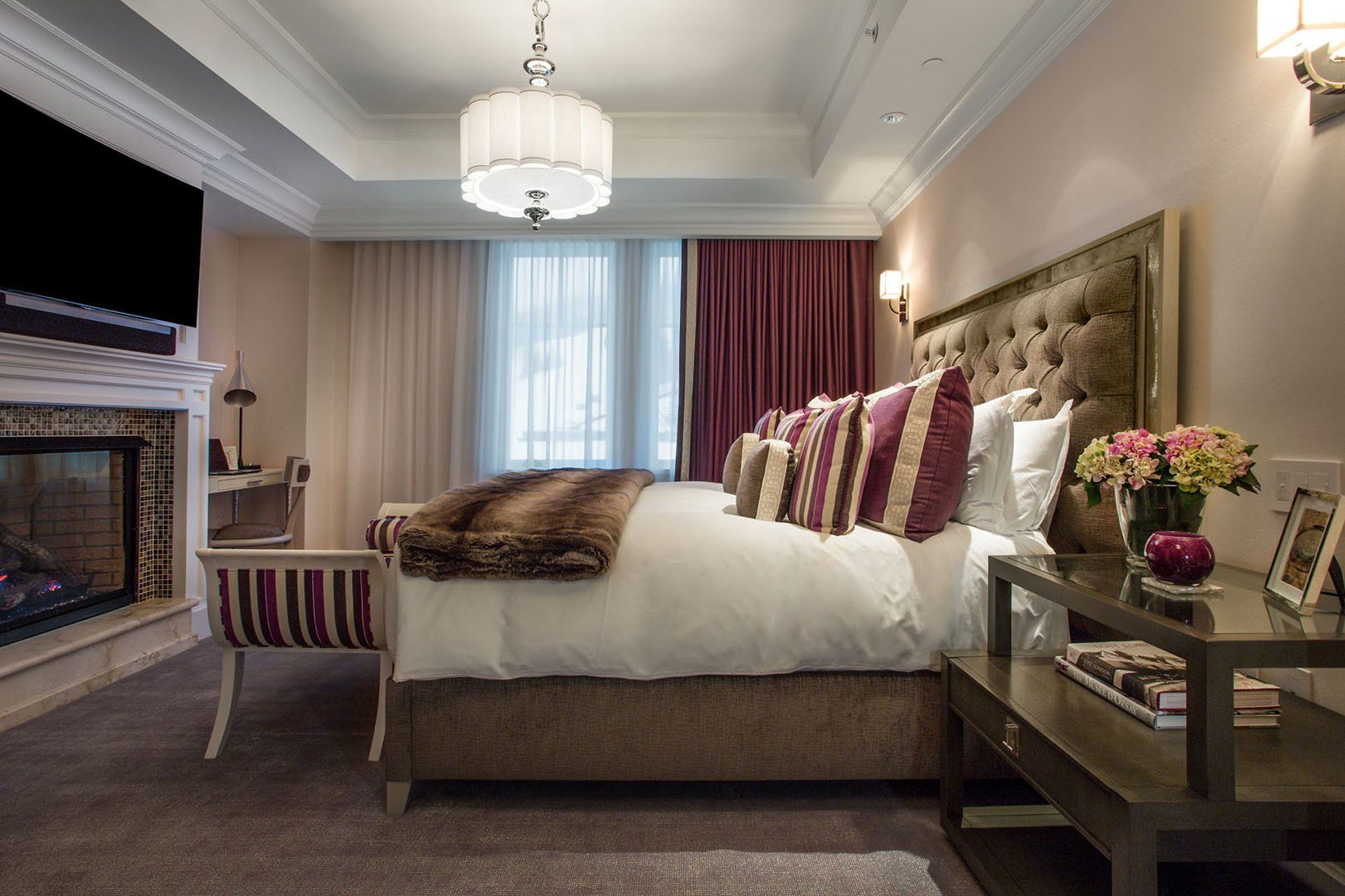 Luxurious bedroom with bed, fireplace, TV, and decorative accents in soft colors.