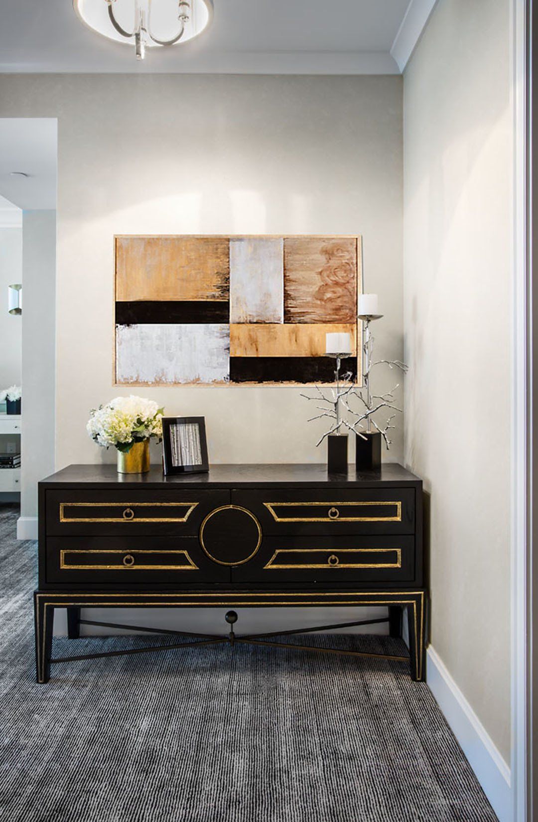 Hallway with black and gold cabinet, abstract art, flowers, and patterned carpet.