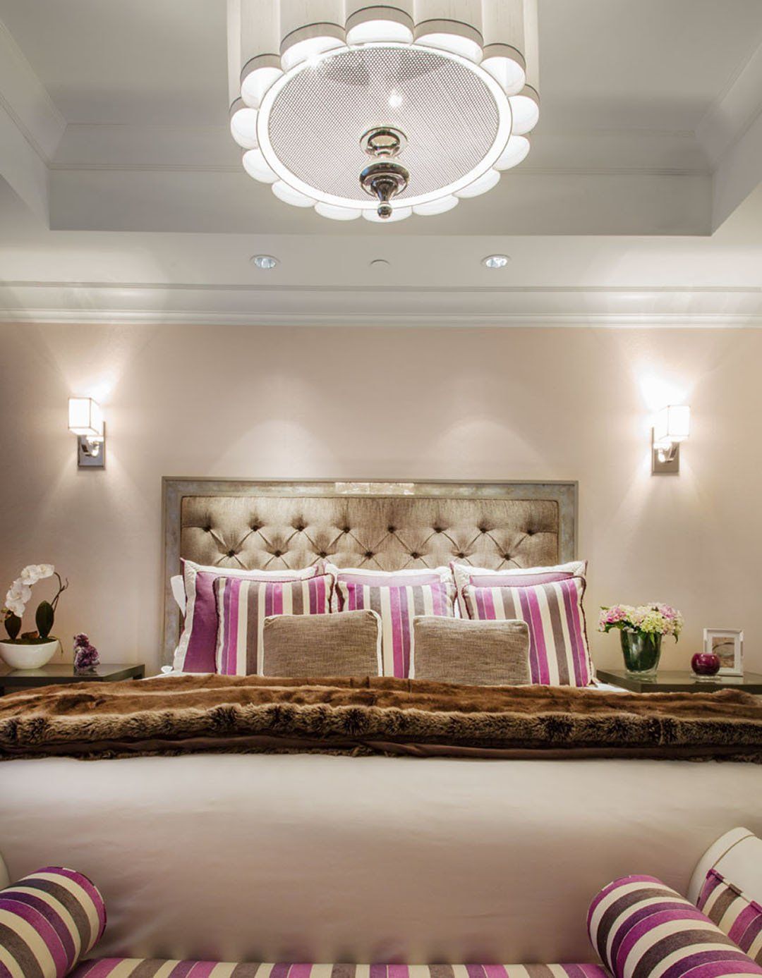 Bedroom with tufted headboard, purple accents, decorative pillows, and a large chandelier.
